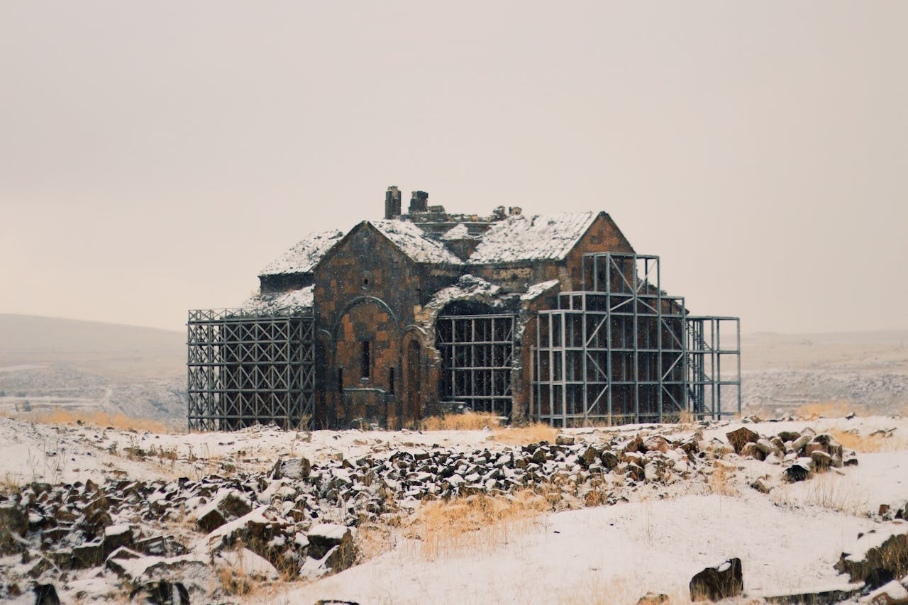 Ancient church ruins with scaffolding amidst a snowy rural landscape.